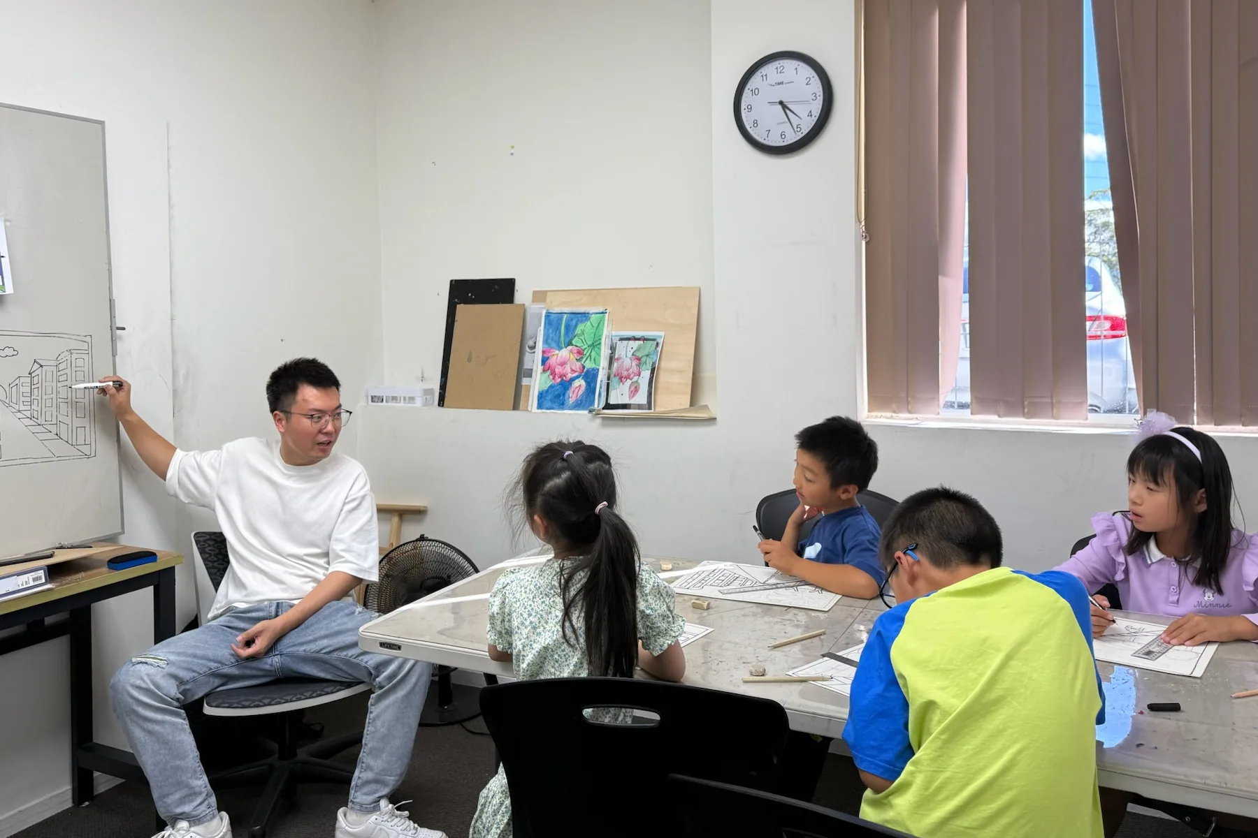 An S&A teacher demonstrating perspective drawing to children around a studio table