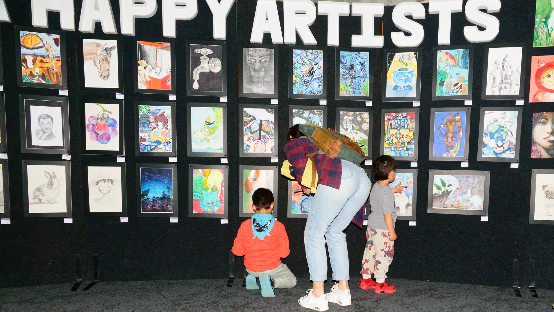 A family seen from behind looking at an S&A Happy Artists wall filled with student artworks