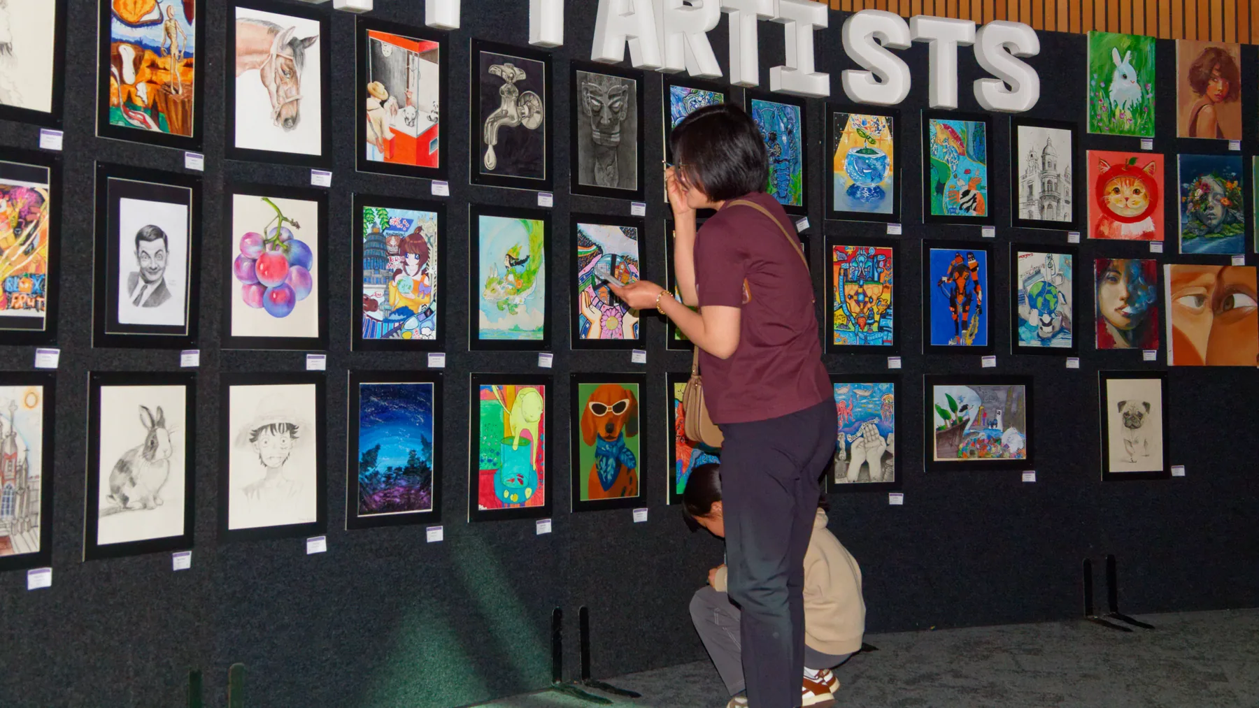 Visitor studying a wall of S&A student artworks at an exhibition