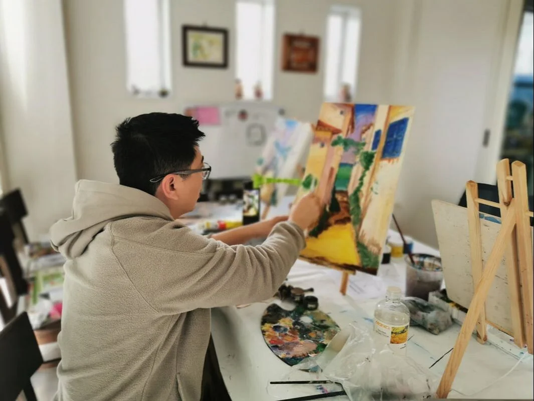 A learner painting architecture on canvas at an easel in an S&A classroom