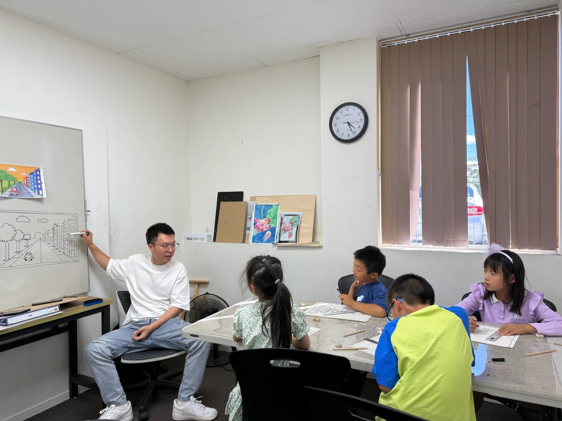 An educator explaining perspective on a whiteboard while students draw at a studio table