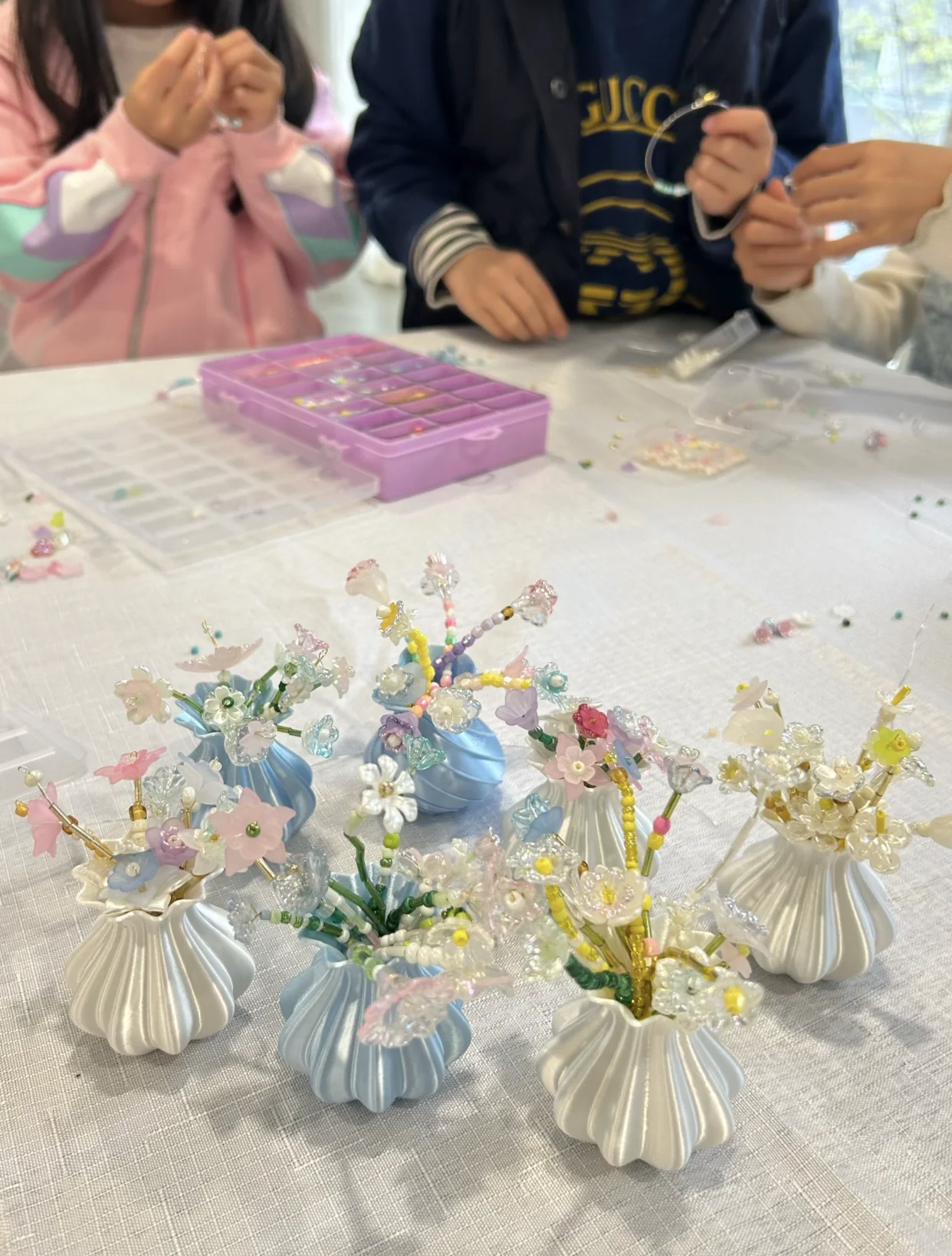 Learners threading colourful beads beside finished beaded flowers in small sculptural vases