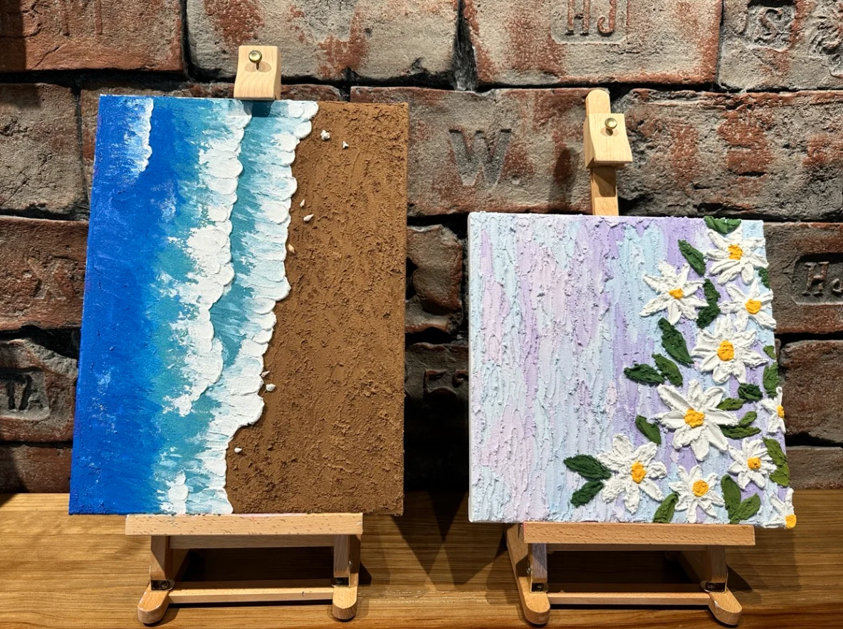 Two small finished relief paintings using raised texture to create a shoreline and flowers